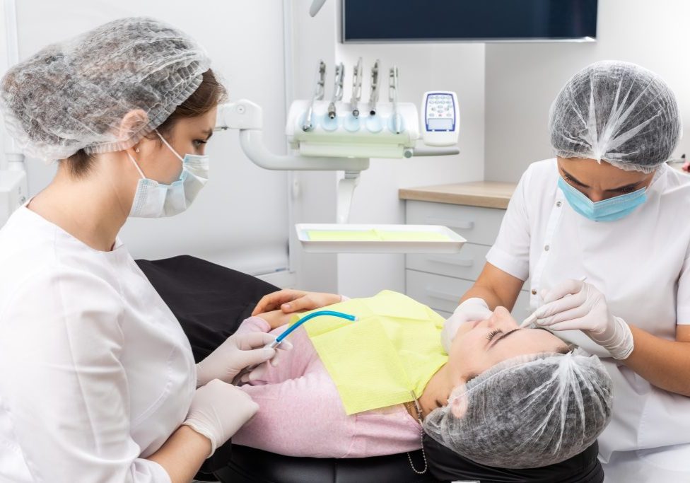 Dentist and assistant performing dental treatment inmodern dental clinic, patient laying in a chair